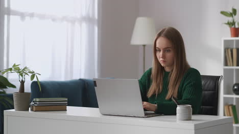 young-student-woman-is-working-with-laptop-in-living-room-of-her-apartment-at-daytime-communicating-by-chat-in-internet-user-of-social-networks